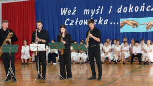 kwartet muzyczny gra na scenie, a w tle siedzą uczniowie z chóru szkolnego