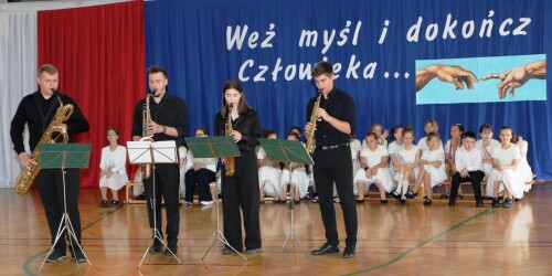 kwartet muzyczny gra na scenie, a w tle siedzą uczniowie z chóru szkolnego