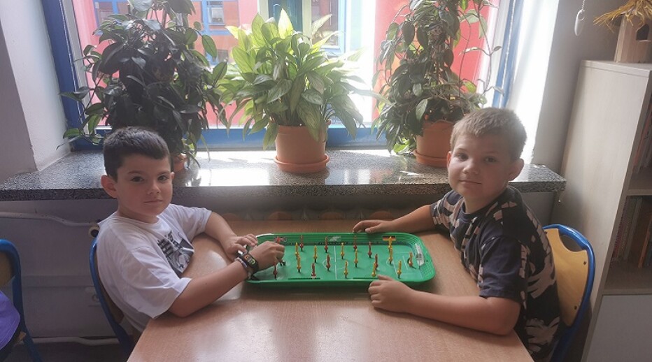 Dwóch uczniów gra przy stole w piłkarzyki